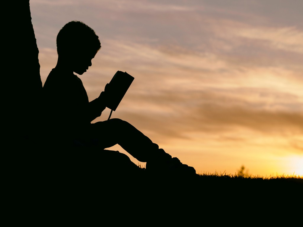 child is being bullied. bullying. bullied at school. boy reading in sunset.