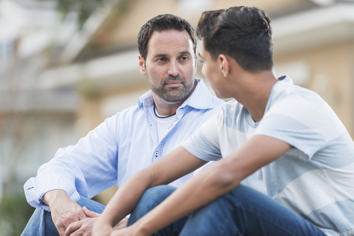 Father Sitting With Serious Teenage Boy