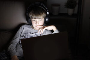 Boy Using Laptop On Sofa At Night